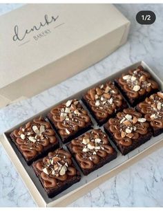 a box of brownies with chocolate frosting and nuts on top sitting on a marble counter