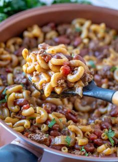 a ladle full of chili macaroni and cheese being held by a spoon