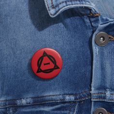 a red button with black letters on it sitting in the back pocket of a jean jacket