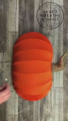 an orange round pillow sitting on top of a wooden floor next to a person's hand