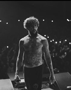 a man with no shirt on standing in front of a stage full of people and lights