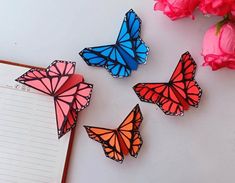 three butterflies sitting on top of a table next to a notepad and pink flowers