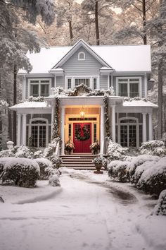 a white house covered in snow with a red door and wreath on the front entrance