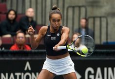 a woman swinging a tennis racquet at a ball with people watching in the background