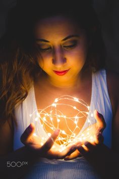 a woman holding a glowing ball in her hands with the light shining on her face