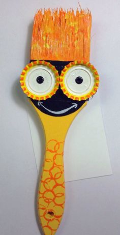 an orange and yellow brush with googly eyes on it's head, sitting on top of a piece of paper