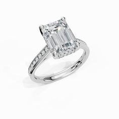 an emerald cut diamond ring with diamonds on the band and shoulders, set in 18k white gold