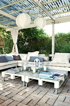 an outdoor living area with couches, tables and lanterns hanging from the pergolated roof