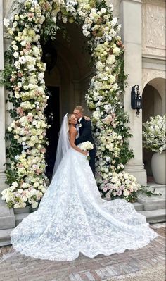 a bride and groom standing in front of a floral arch with white flowers on it