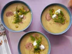 three bowls filled with soup on top of a purple tablecloth next to an orange and white napkin