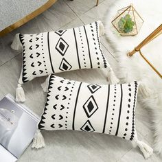 two black and white pillows with tassels sitting on the floor next to a coffee table