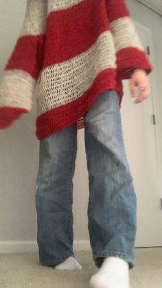 a person standing in front of a door wearing jeans and a red sweater with white stripes