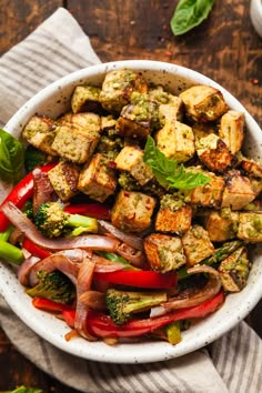 a white bowl filled with tofu, broccoli and red peppers on top of a wooden table