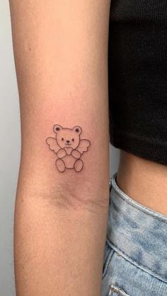 a small teddy bear tattoo on the left arm and right arm behind her is a woman's stomach