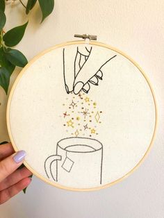 someone is holding up a embroidery hoop with a coffee cup and stars coming out of it