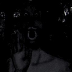 a man with his mouth open in the dark holding something up to his face and making a creepy face