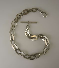 This is a low grade silver chain. What does that mean? Most silver chains we sell are English silver with clear hallmarks on every link. We also sell fancier chains which may be stamped Sterling. This chain has no silver marks. So we test it with acid for its purity and in this case get a low testing. So the silver content in the chain did not have enough to earn some sort of stamp. The chain is still an antique silver chain but the low grade purity is represented in the price. This is a massive chain which weighs 114g and measures 430mm in length. The chain is made up of a single length of large curb links with the largest being 19mm by 14mm. The chain also has an oversized dog clip and T bar - I have taken comparison shots of a regular sized dog clip and T bar to give you an idea of size Silver Oval Chain Necklace For Formal Occasions, Victorian Silver Chain Jewelry, Antique Silver Link Necklace, Classic Silver Necklace With Hook And Links, Silver Engraved Chain Necklace For Formal Occasions, Silver Hallmarked Oval Link Chain Necklace, Vintage Silver Engraved Chain Necklace, Vintage Silver Curb Chain Jewelry, Antique Silver Chain Necklace