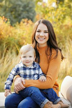 a woman holding a small child in her lap and smiling at the camera while sitting on a bench