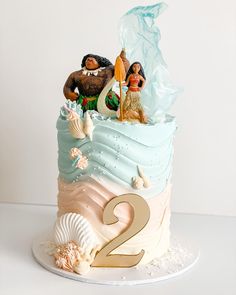 a two tiered birthday cake decorated with figurines and seashells on top