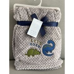 a gray and blue towel wrapped in knit with a dinosaur design on the front that says, let's roar