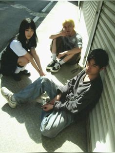 three young people sitting on the side of a building