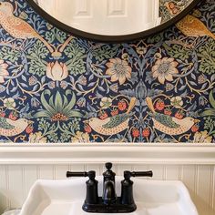 a bathroom sink sitting under a mirror next to a wall mounted faucet with birds and flowers on it