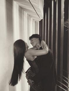 two women hugging each other in front of a window with vertical blinds on the wall behind them