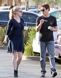 a man and woman walking down the street talking to each other while holding coffee cups