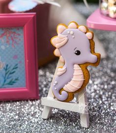 a cookie shaped like a sea horse sitting on top of a wooden stand next to a pink frame