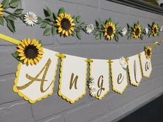 sunflowers and daisies are hanging on the wall next to a name banner