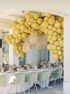 a table with yellow balloons hanging from it's ceiling and green chairs around it