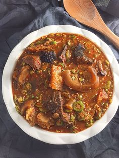 a white bowl filled with meat and vegetables on top of a table next to a wooden spoon