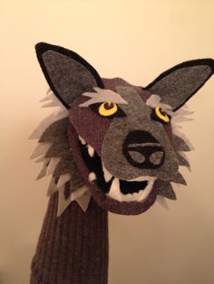 an animal head made out of felt with yellow eyes and mouth, on a white wall