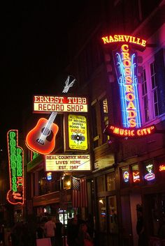 people walking down the street at night in front of neon signs and music storefronts