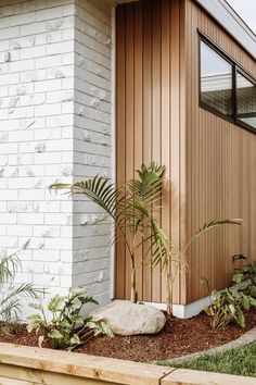 a white brick house with wood siding and plants in the foreground, next to a wooden planter box