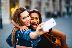 two young women taking a selfie with their cell phone while walking down the street