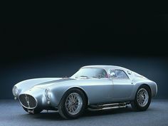 an old silver sports car sitting on top of a gray floor in front of a black background