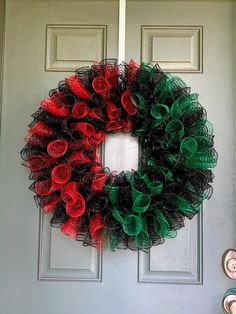 a wreath with red, green and black mesh on the front door to a house