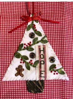 a christmas tree made out of fabric with buttons and holly leaves on the top, sitting on a red checkered tablecloth