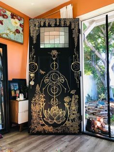 a black door with gold designs on it in front of an orange wall and wooden floor