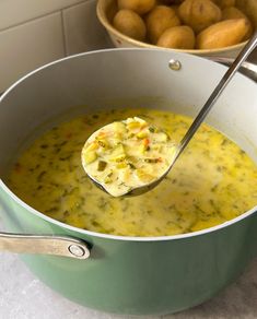 a ladle full of soup with potatoes in the bowl and another bowl behind it