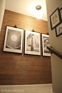 three framed pictures hang on the wall next to a stair case with wooden slats