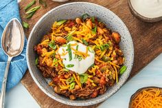 a bowl filled with chili, beans and sour cream on top of a wooden cutting board