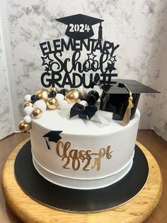 a white cake with gold decorations and a black graduation cap on top that says elementary school graduate