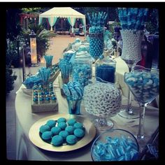 a table topped with lots of blue and white desserts next to tall glass vases filled with candy