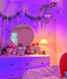 a bedroom decorated in pink and purple with flowers on the dresser, mirror and lamp