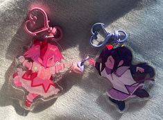 two keychains that are shaped like cartoon characters, one is pink and the other is purple