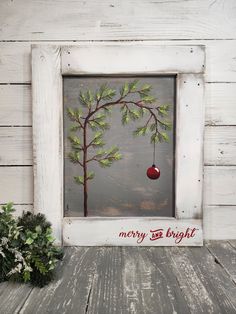 a white frame with a christmas ornament hanging from it's side next to a potted plant