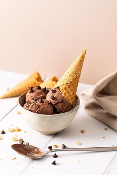 two scoops of ice cream in a bowl with chocolate chips on the side and an ice cream cone sticking out of it