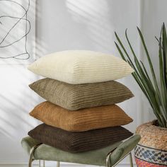 a stack of four pillows sitting on top of a chair next to a potted plant